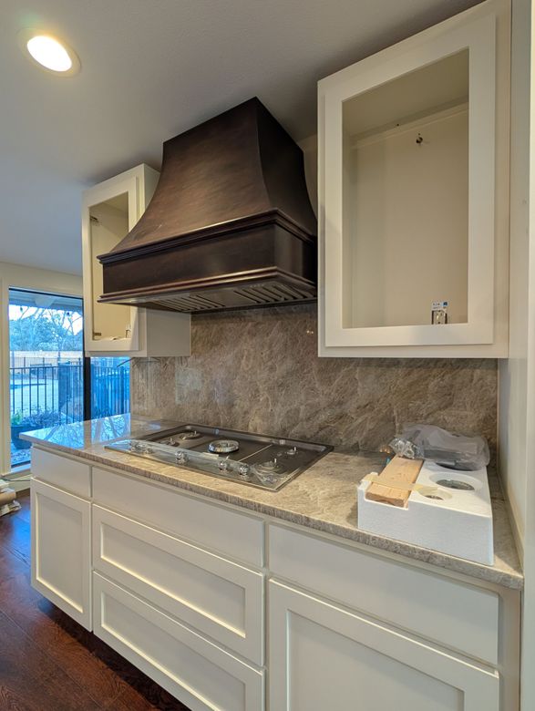Kitchen with white cabinets, dark range hood, and tile backsplash.