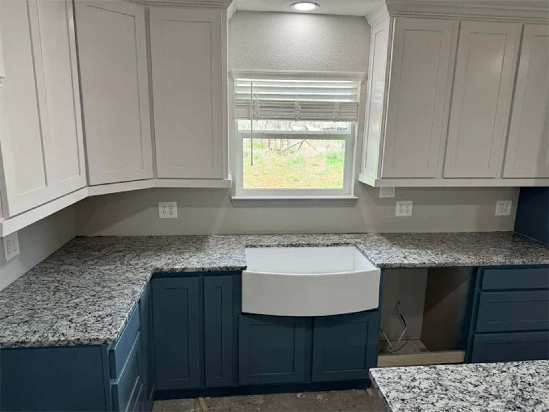 Bright kitchen with granite countertop, sink, and modern chrome faucet. Living room with couches visible through windows.