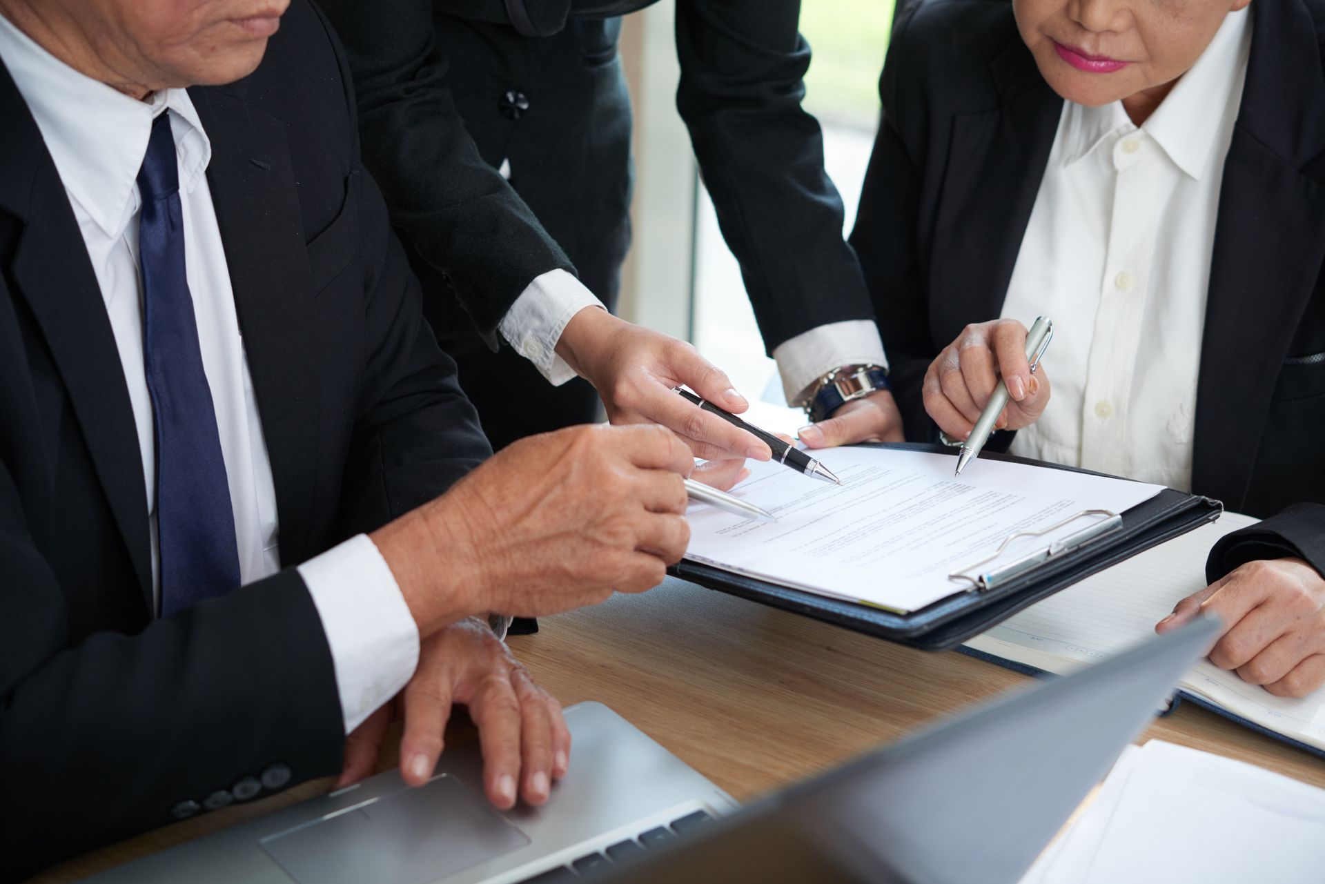 A group of business people are sitting at a table looking at a clipboard.
