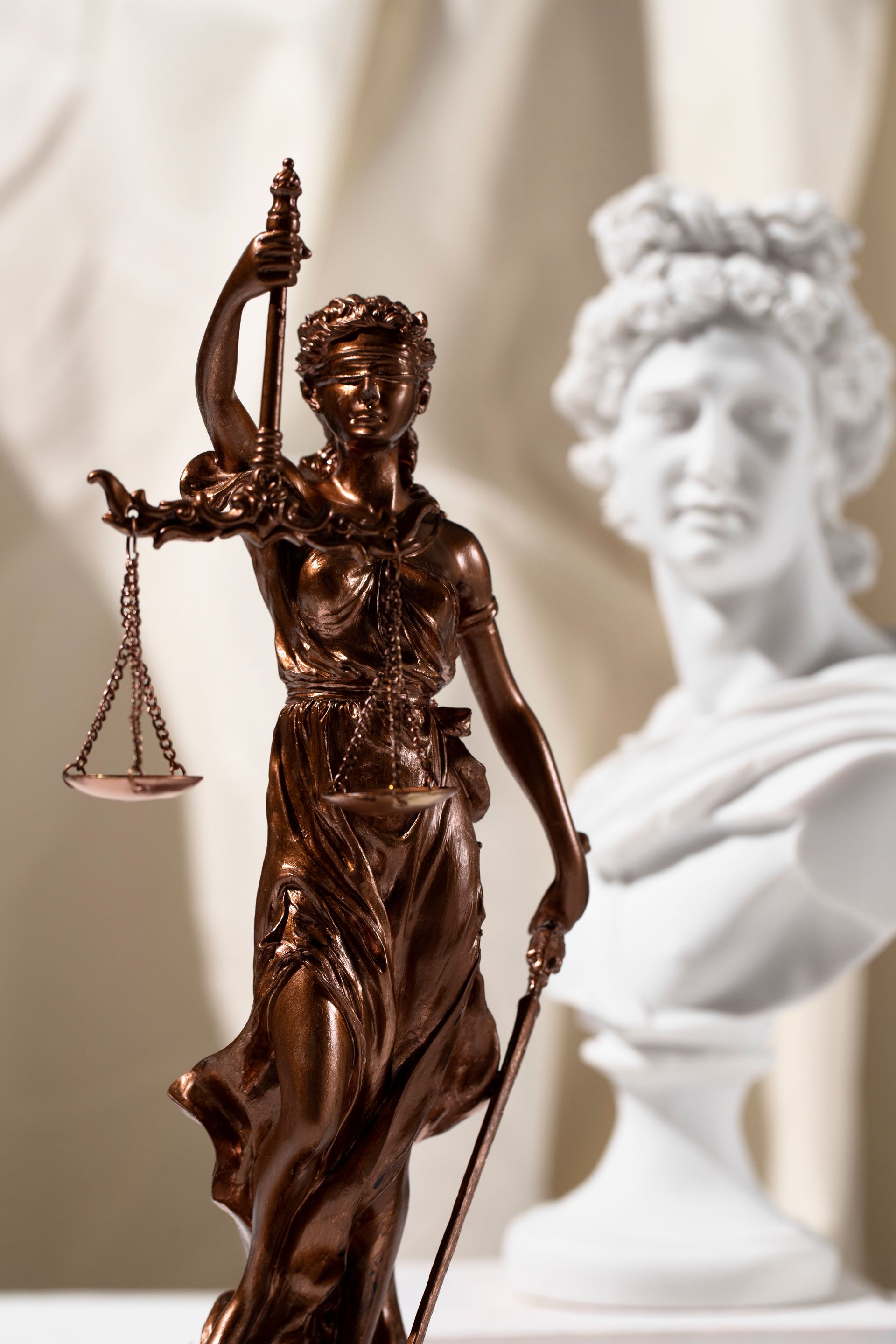 A statue of a woman holding scales of justice next to a bust of a woman.