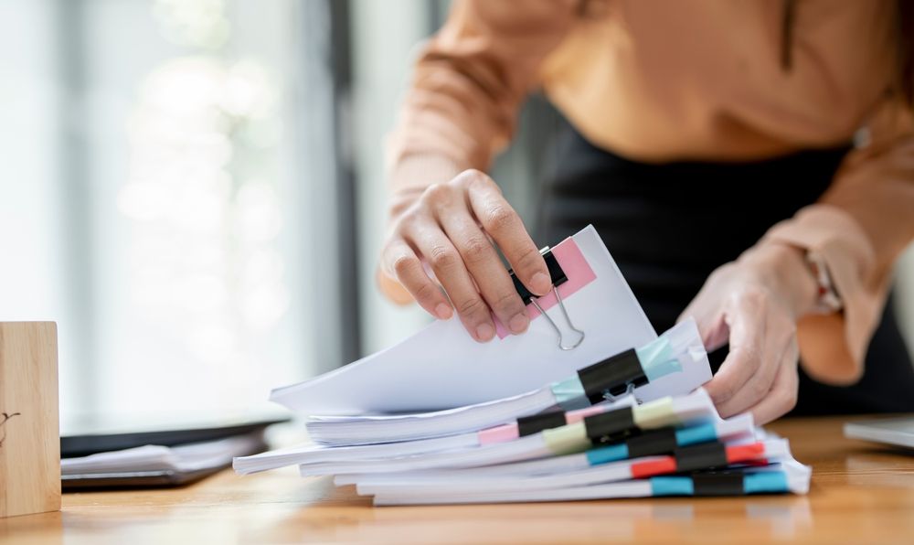 A woman is holding a stack of papers on a table.