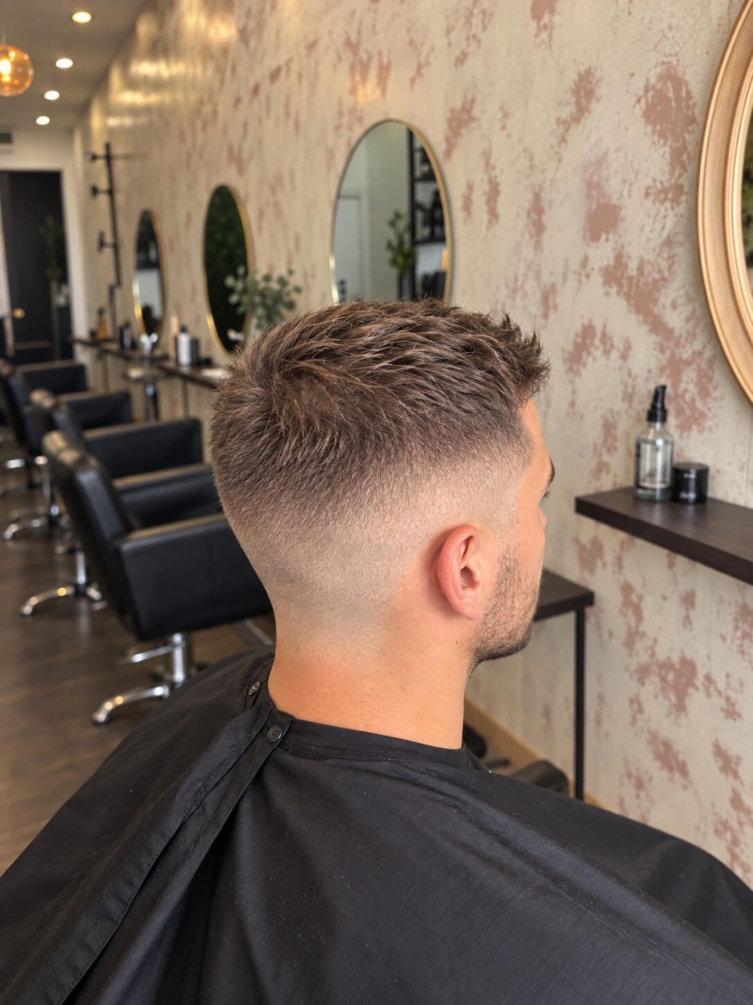 Hombre con corte de pelo corto degradado sentado en una silla de barbero dentro de un salón moderno.