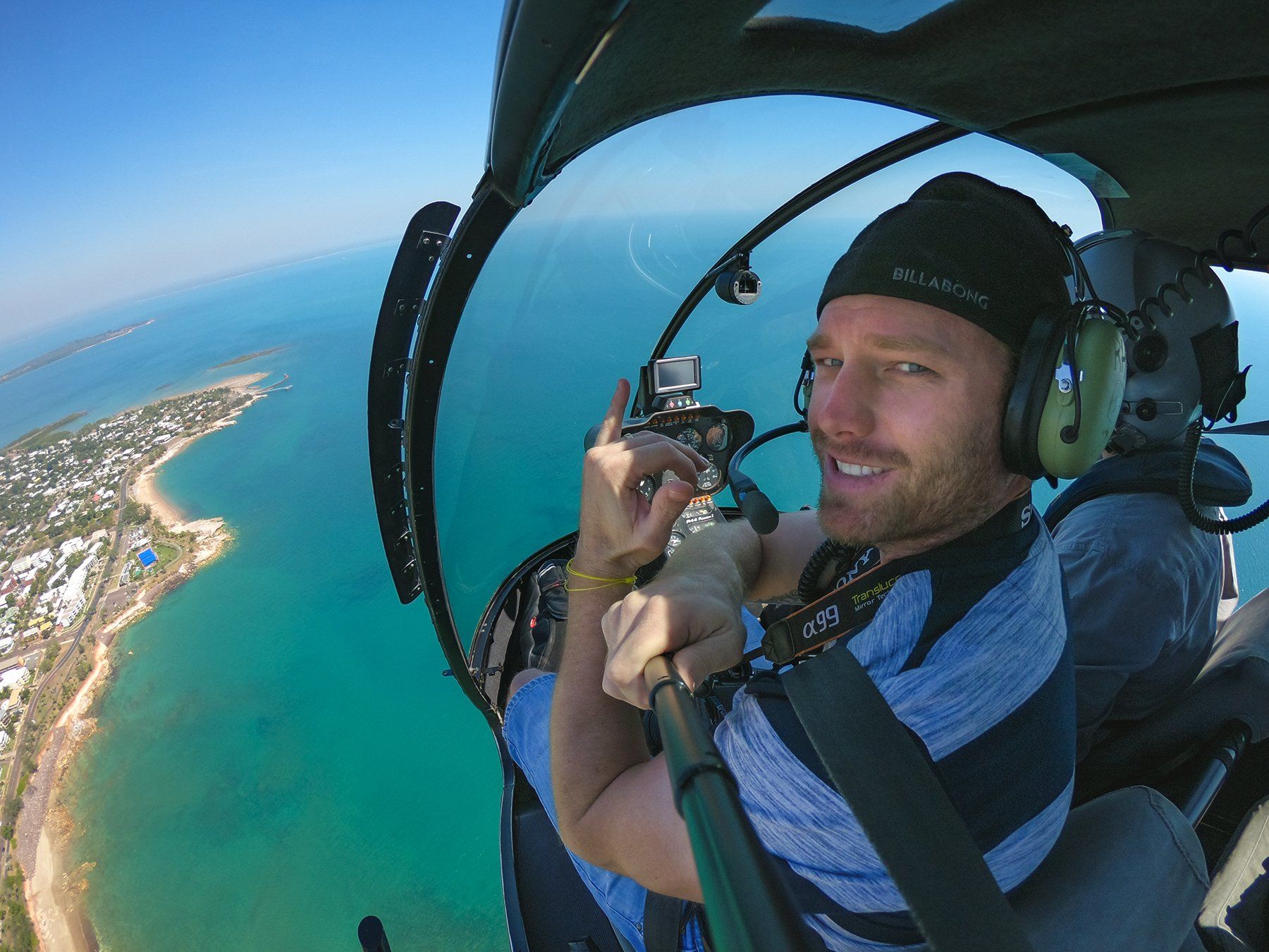 A man is sitting in the cockpit of a helicopter over the ocean.
