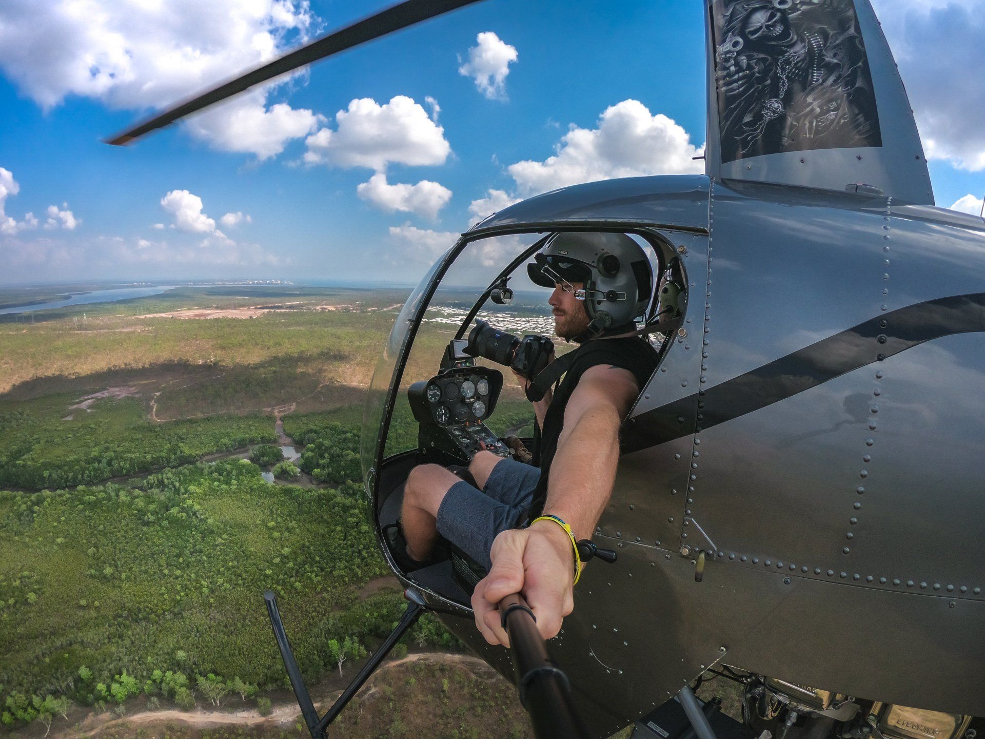 A man is taking a selfie while flying a helicopter over a forest.