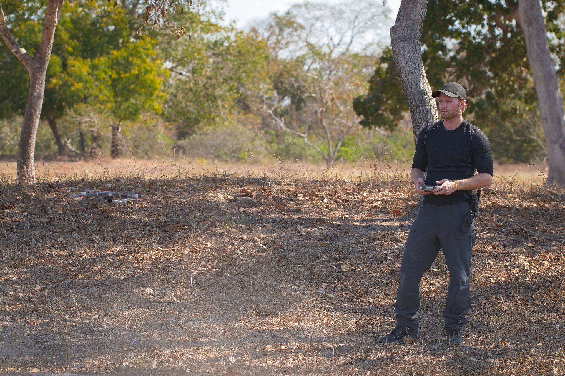 A man is standing in a field holding a remote control.