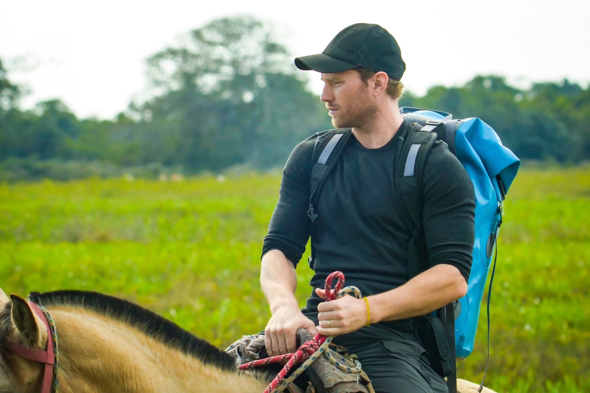 A man with a backpack is riding a horse in a field.