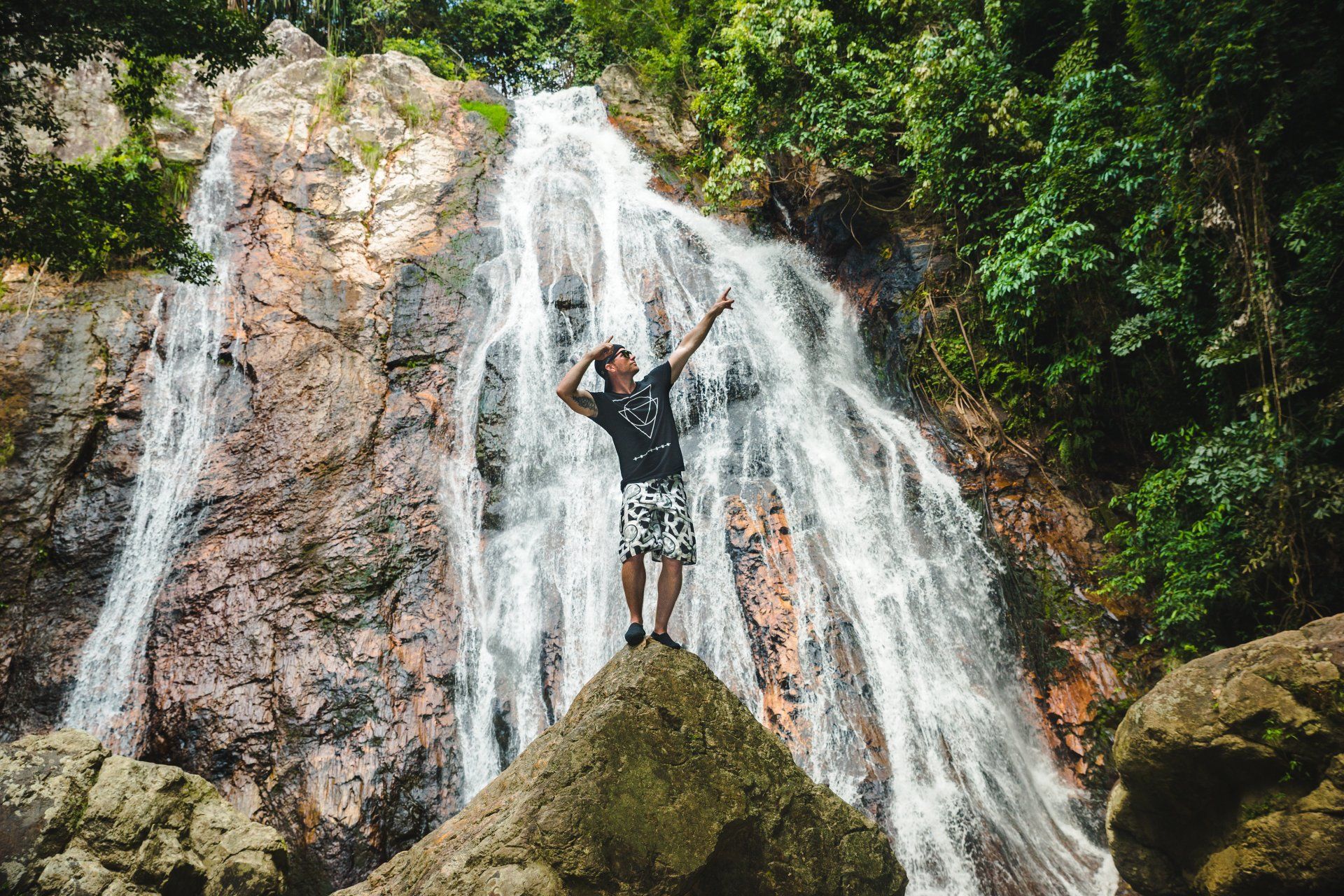 A man is standing on a rock in front of a waterfall.