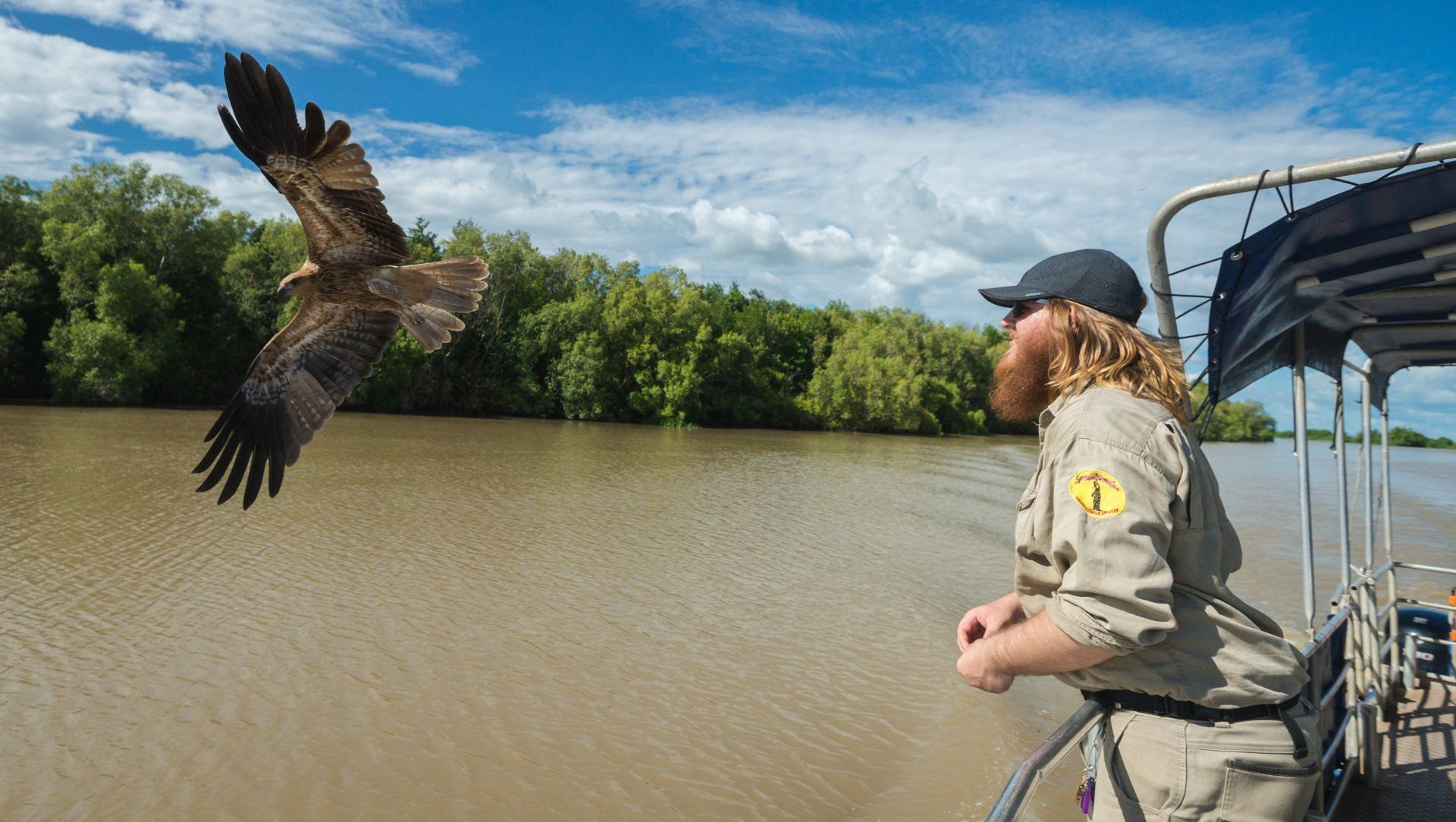 A man is standing on a boat watching a bird flying over the water.
