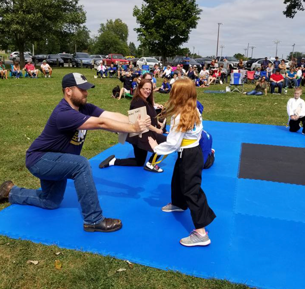 A man and a girl are kneeling on a blue mat in a park