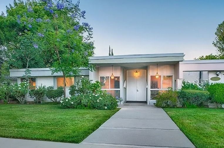 Mid-century modern home with a flat roof, large windows, and manicured lawn. Blue tree and greenery.