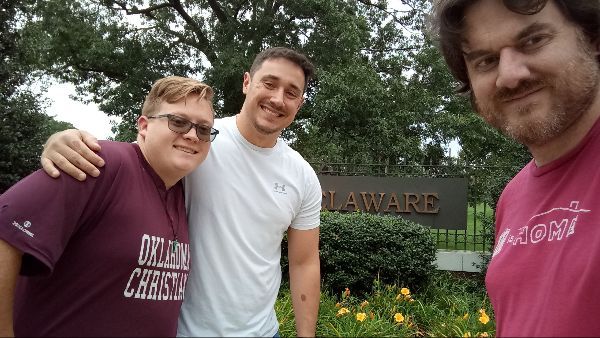 Three men are posing for a picture in front of a sign that says leward