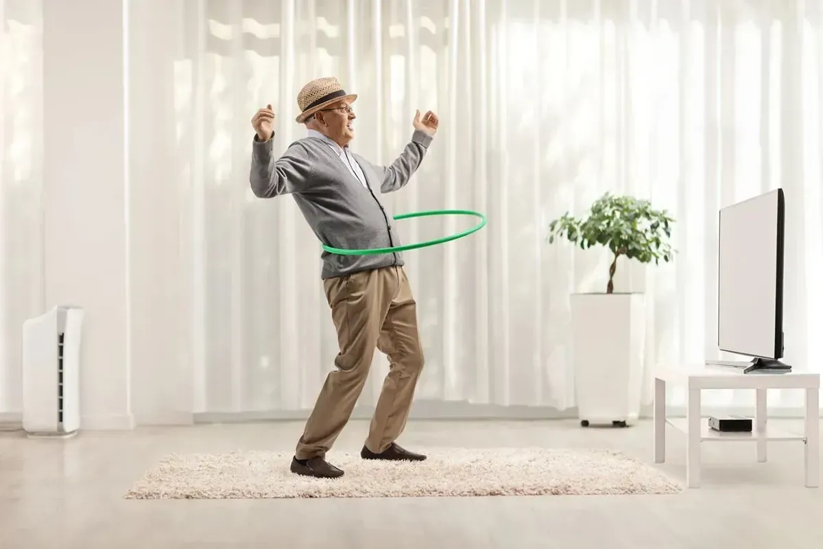 Senior man hula hooping in his living room.