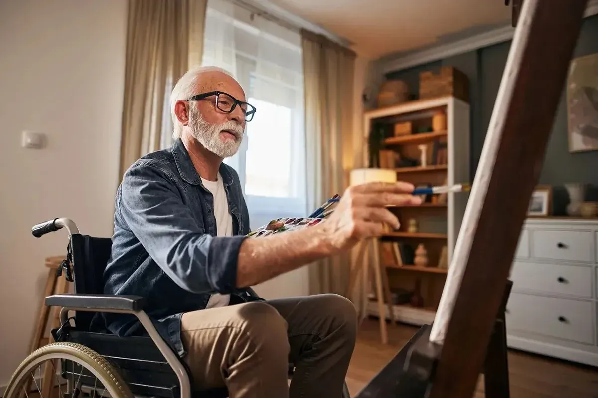 Man in a wheelchair, painting at home.