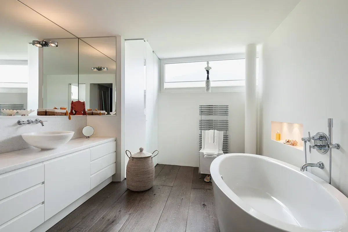 Wide, long and dark engineered hardwood flooring planks in a white small bathroom with bathtub.