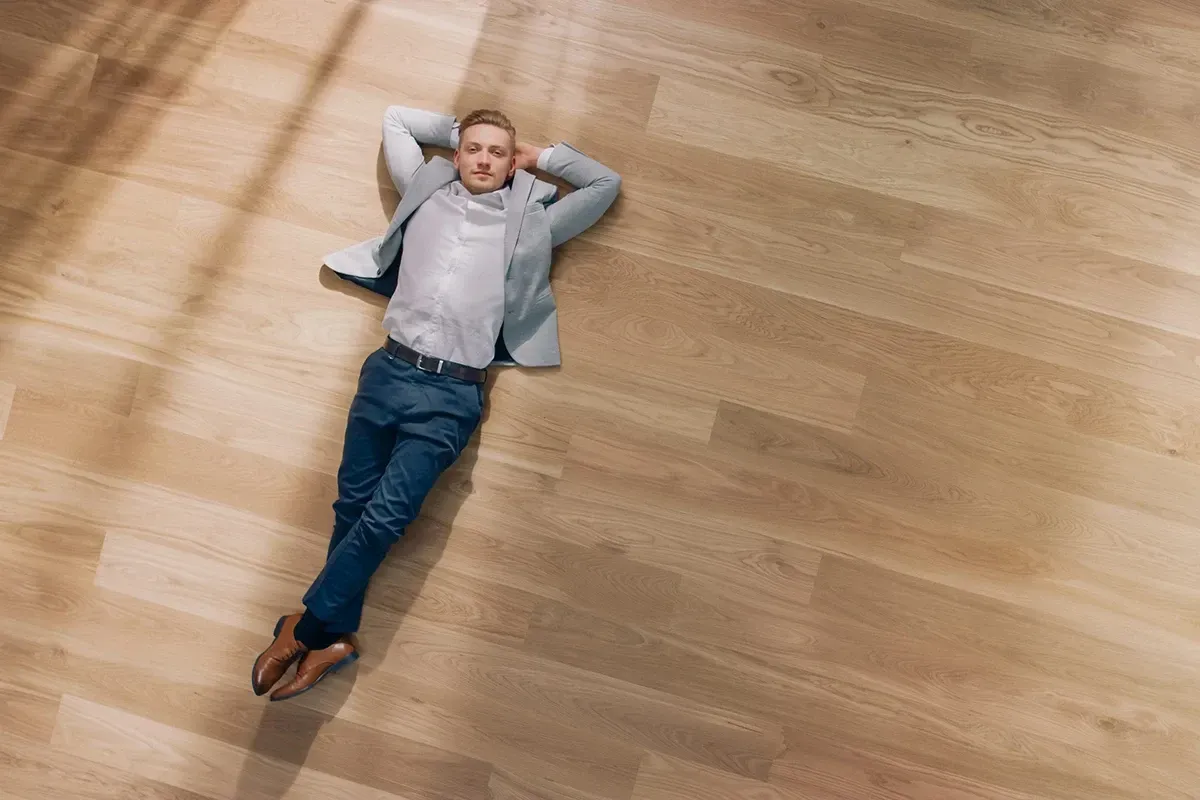 Young, well-dressed man laying down on a hardwood floor.