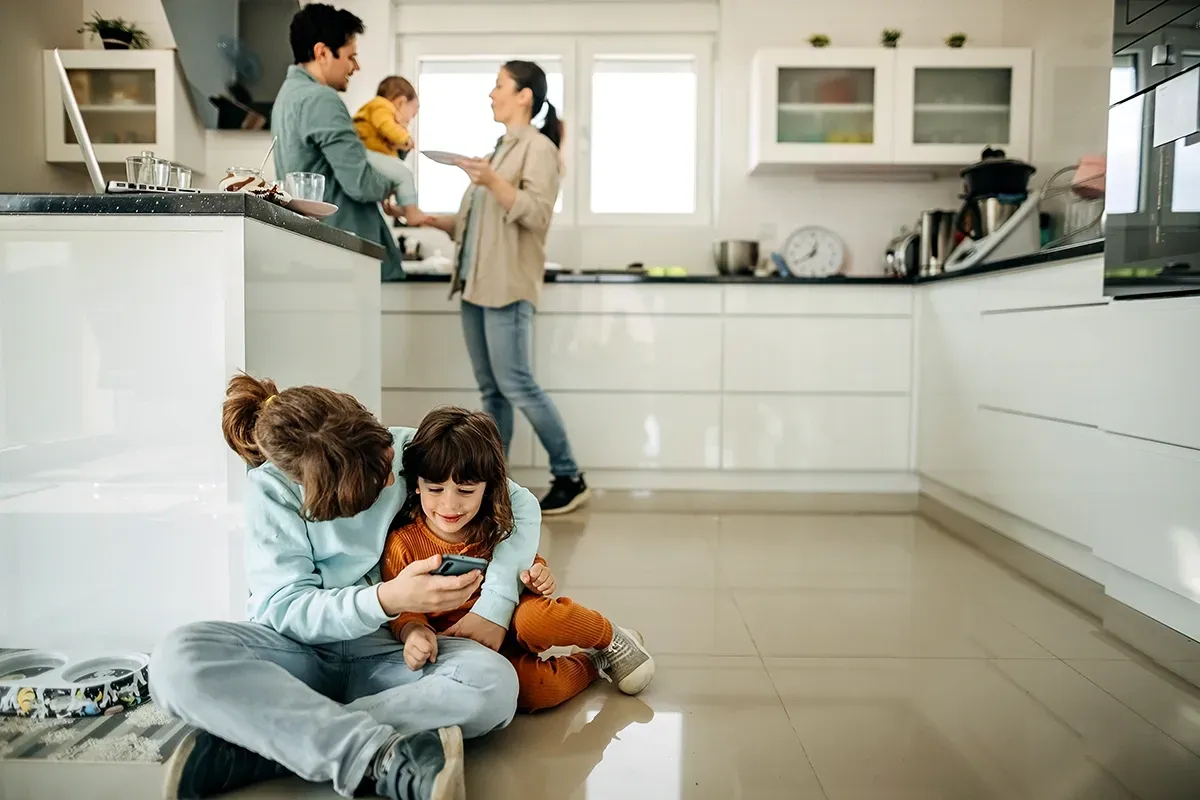 Kids sitting on a kitchen floor with parents in the background.