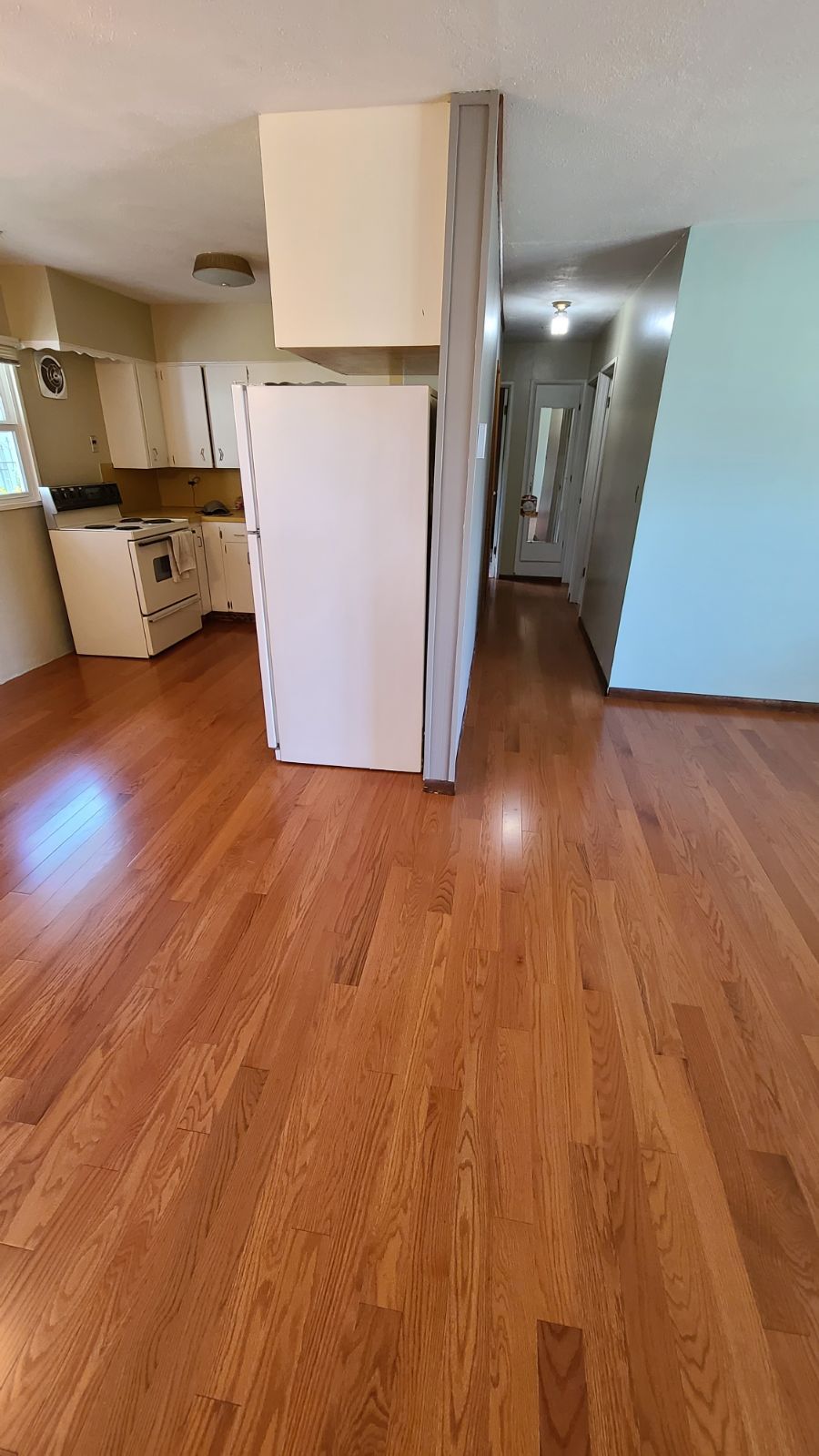 An empty kitchen with hardwood Somerset floors and a refrigerator.