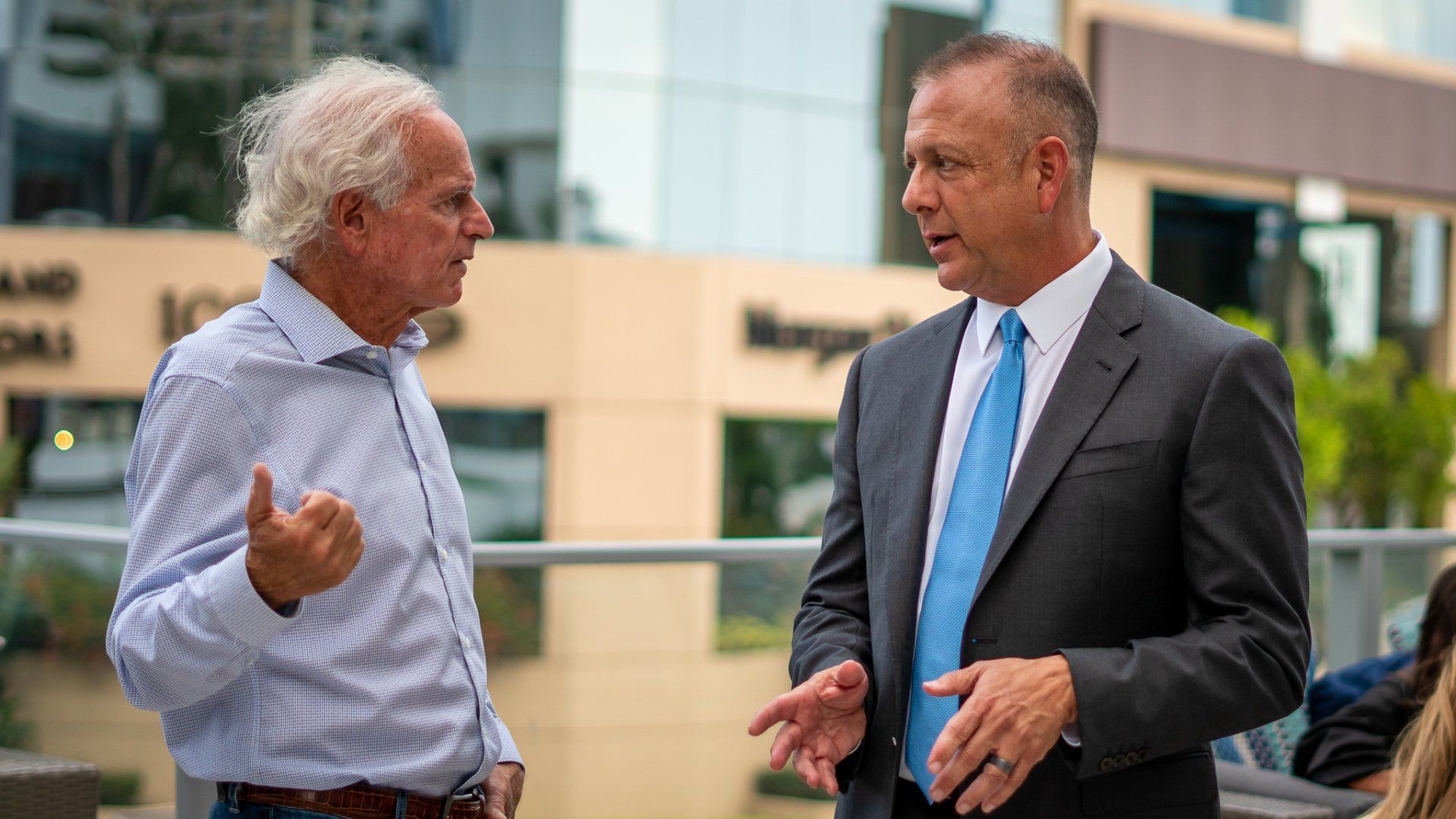 Two men in suits are talking to each other in front of a building.