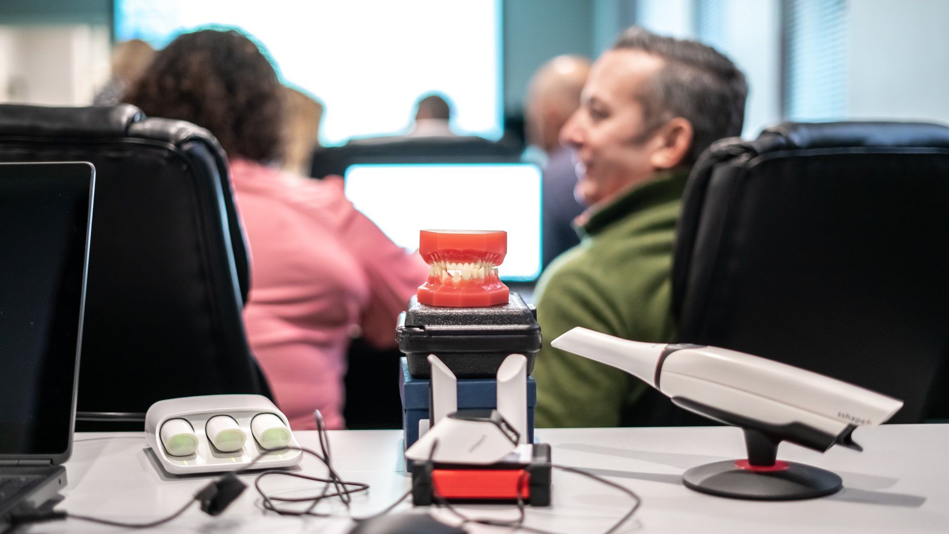 A man is sitting at a desk with a laptop and a model of teeth.