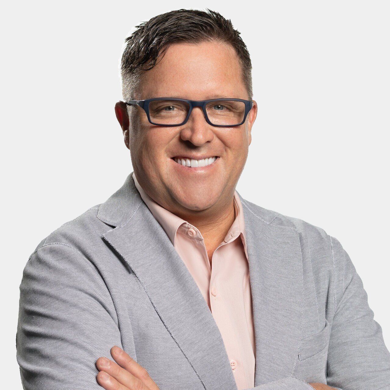 A man wearing glasses and a suit is smiling with his arms crossed.