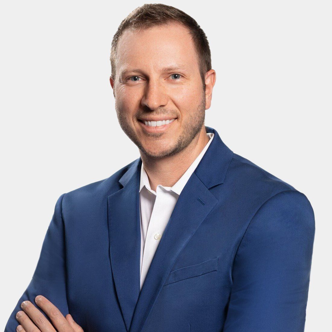 A man in a blue suit and white shirt is smiling with his arms crossed.