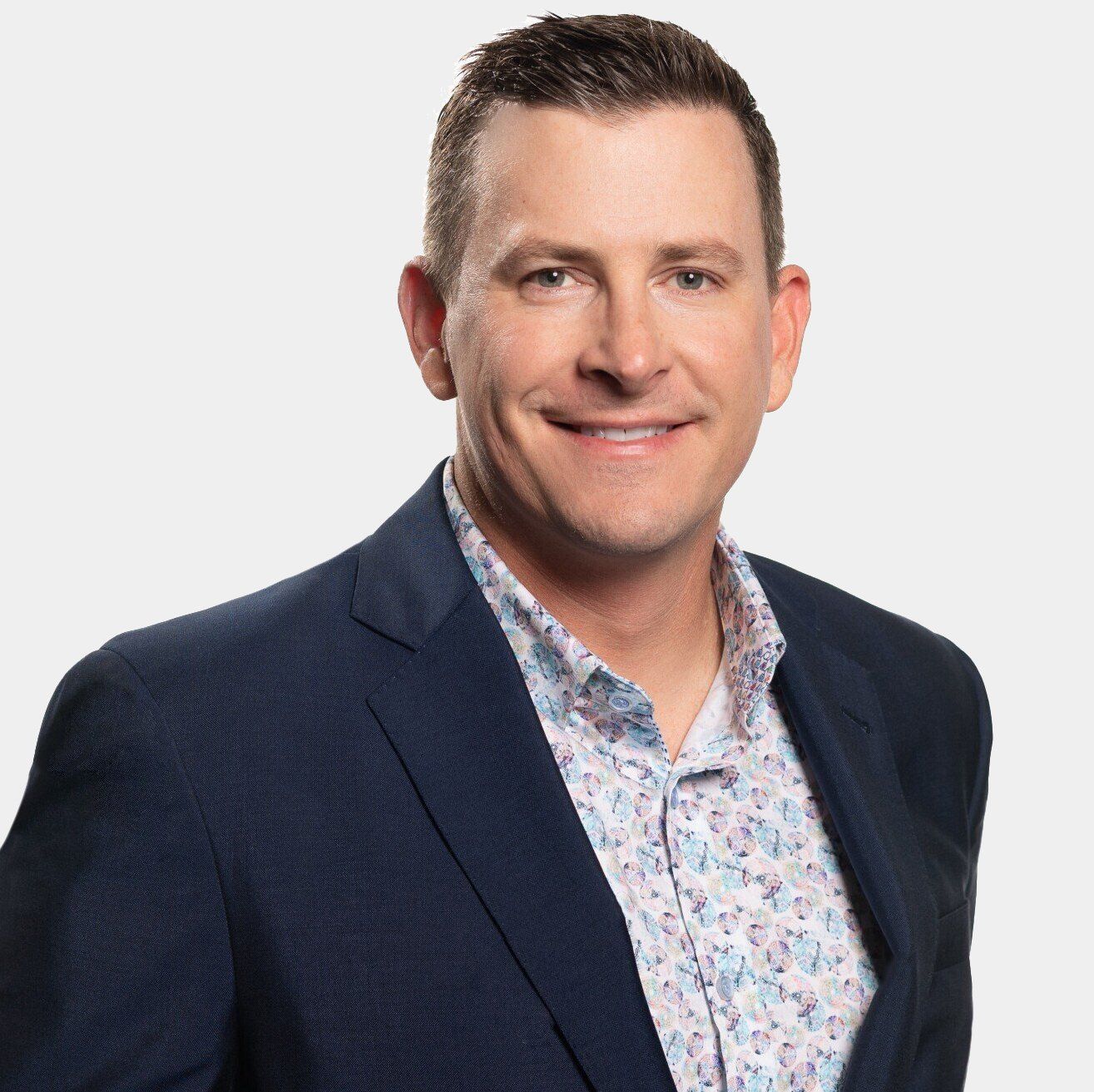 A man in a suit and floral shirt is smiling for the camera.