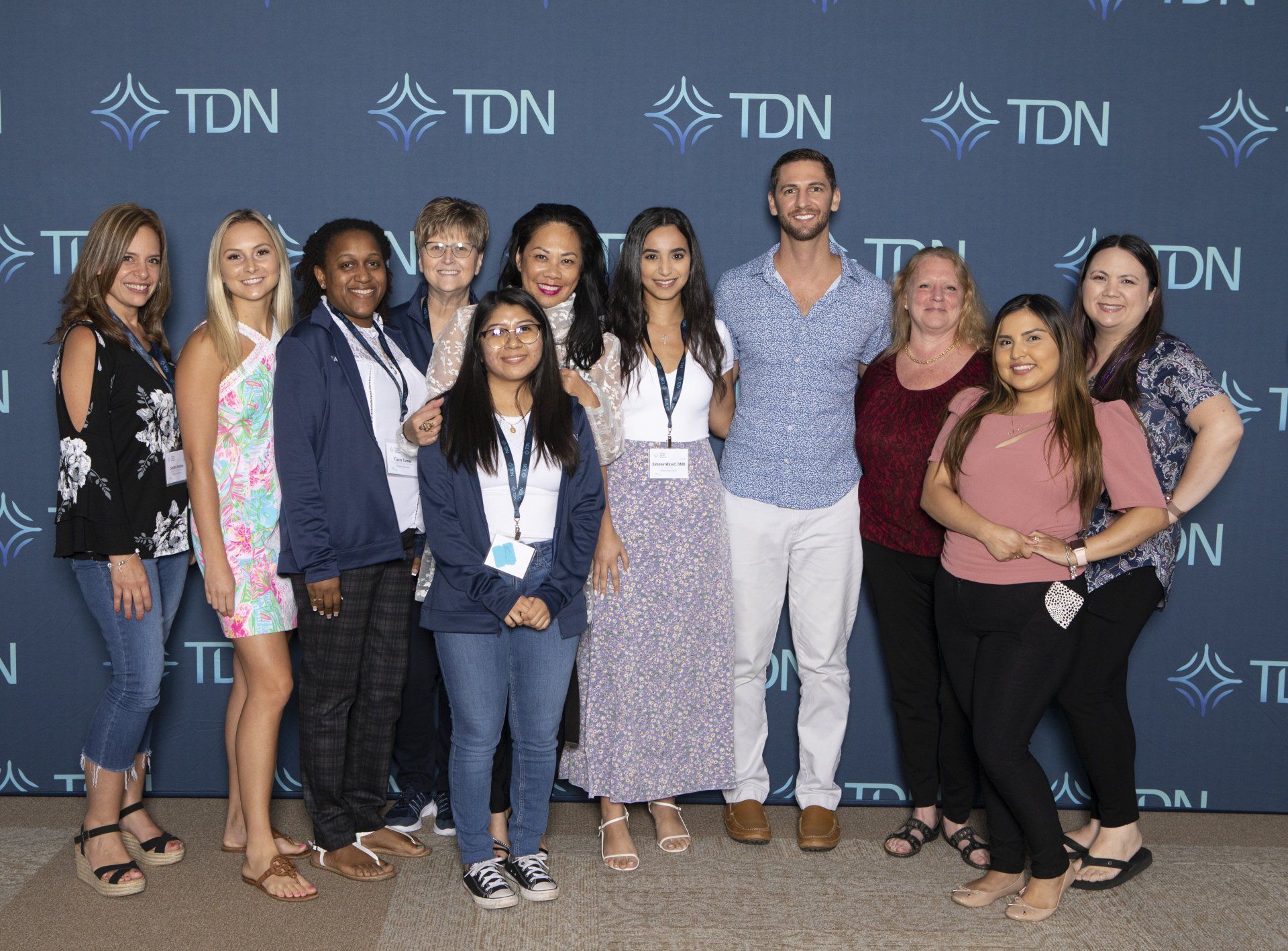A group of people are posing for a picture in front of a wall that says tdn.