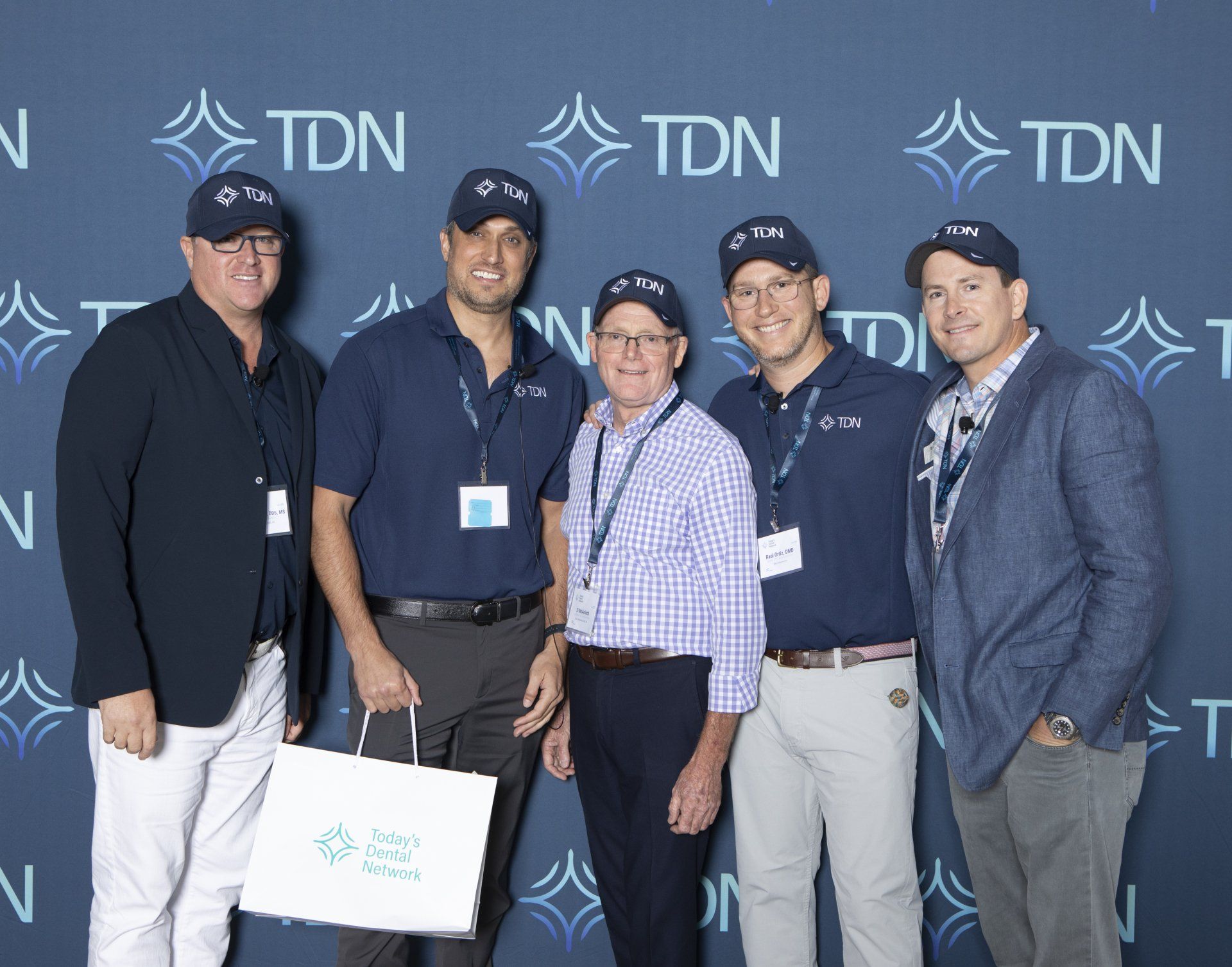 A group of men are posing for a picture in front of a wall that says tdn