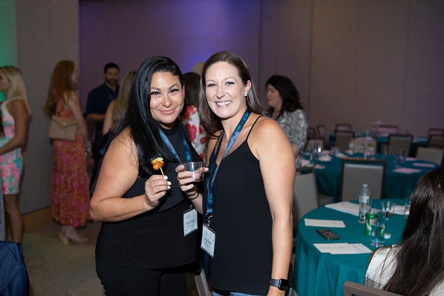 Two women are standing next to each other in a room holding drinks.