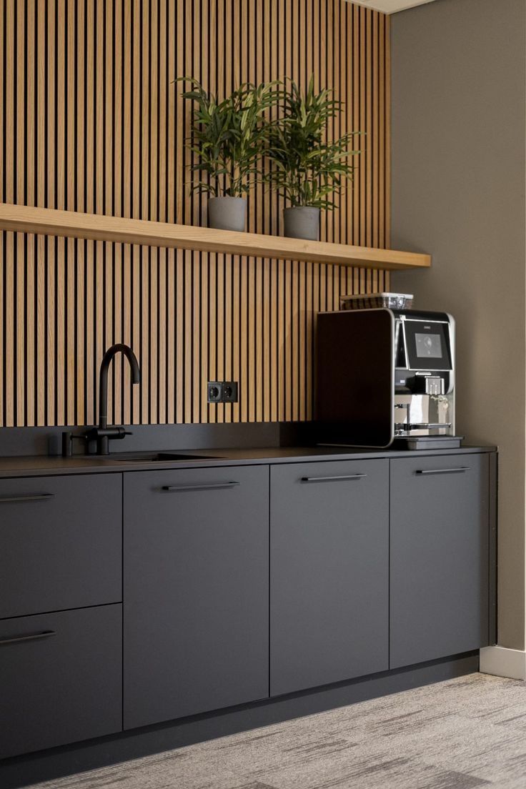Modern kitchen area with black cabinets, a sink, coffee machine, and wooden slat wall.