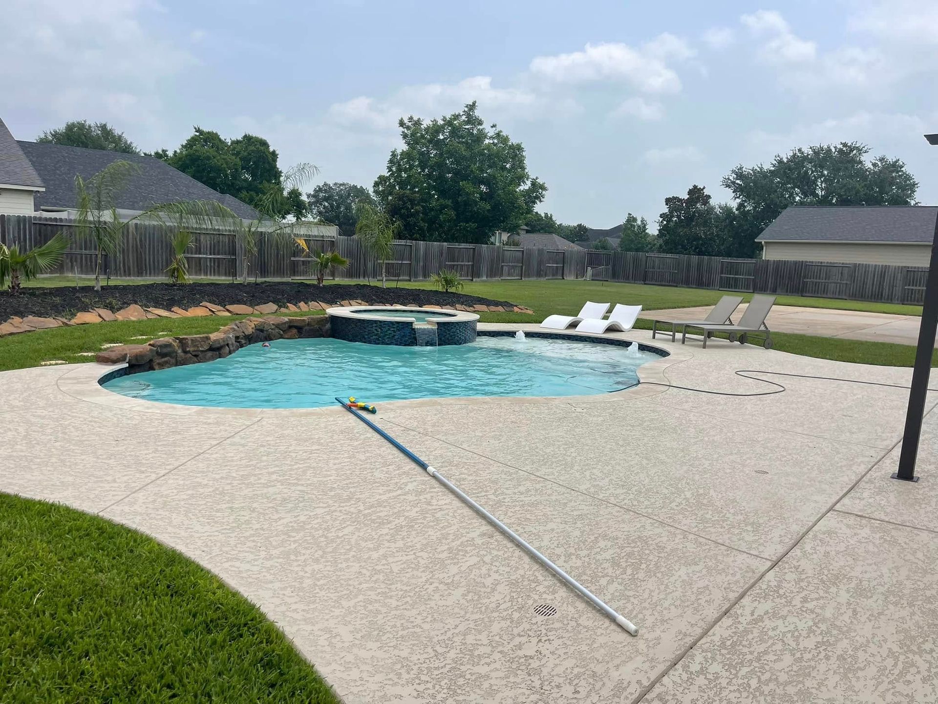 Backyard swimming pool with lounge chairs and a stone patio, featuring a fallen metal pole in the foreground