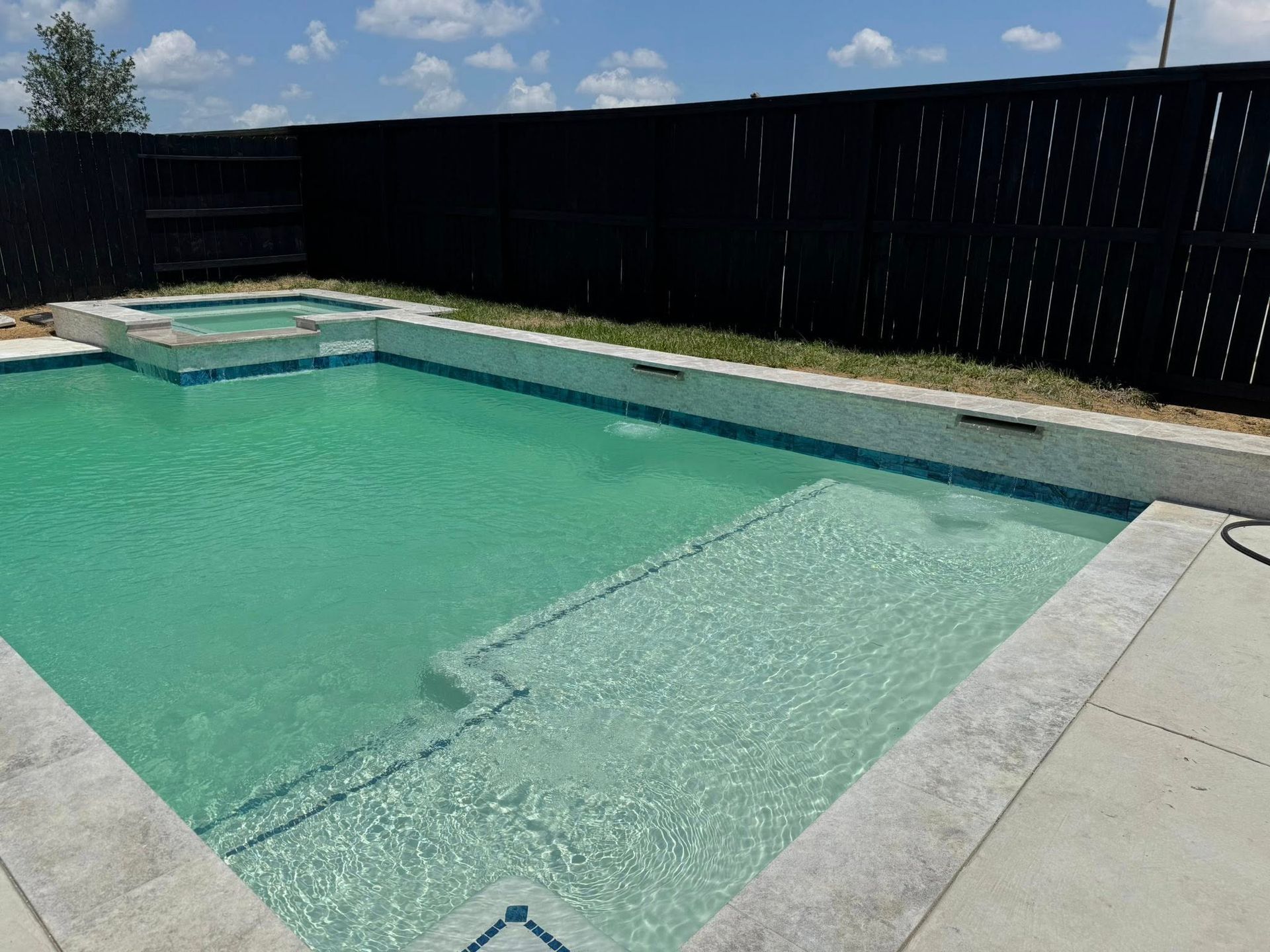 Swimming pool with turquoise water, shallow steps, and a black privacy fence under a sunny sky
