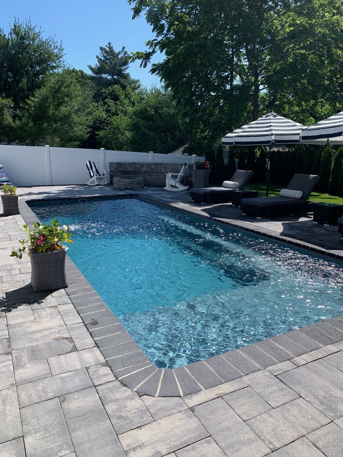 Backyard pool with stone patio, lounge chairs, and striped umbrellas on a sunny day