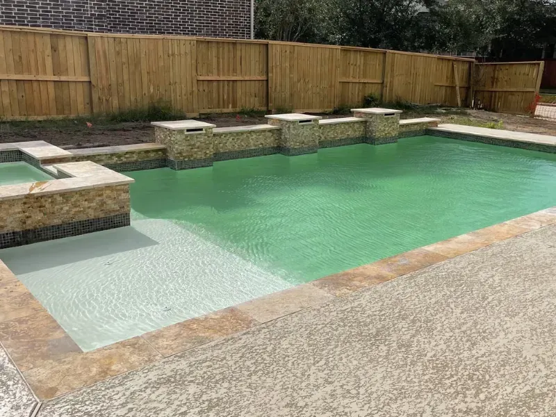 Backyard swimming pool with pale green water, stone steps, and a wooden privacy fence
