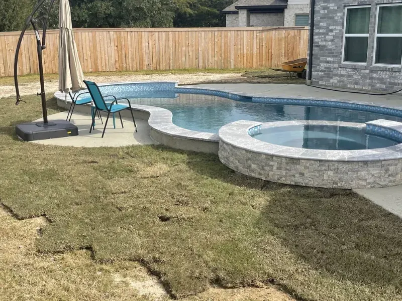 Backyard pool with a raised round hot tub, blue lounge chairs, and a stone patio beside a lawn