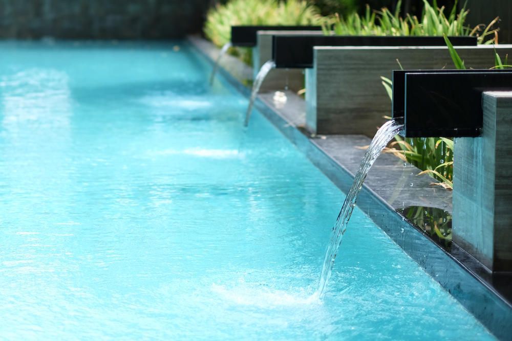 Modern pool with blue water and built-in spouts pouring water along the edge