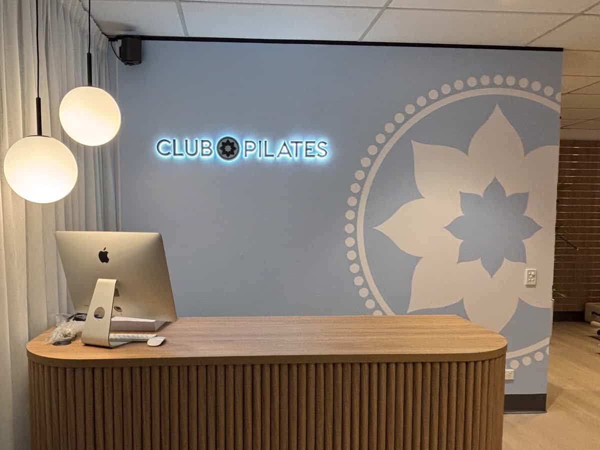 A desk with a computer on it in front of a wall that says club pilates.   — Solis Signs in Toukley, NSW