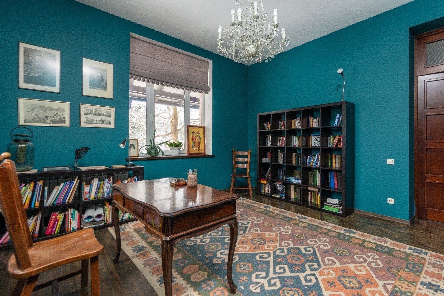 A living room with blue walls , a table , chairs , and a bookshelf.