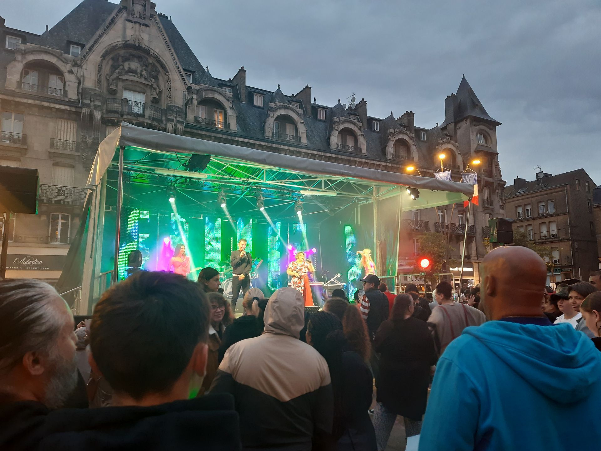 Orchestre Anthracite sur une scène extérieure devant un public, avec éclairages colorés et bâtiment en arrière-plan.