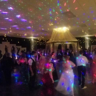Guests dancing at a dimly lit party with colorful disco lights and a gold ceiling centerpiece
