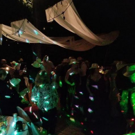 People dancing under draped lights at a dark party, with green glow and confetti-like reflections.
