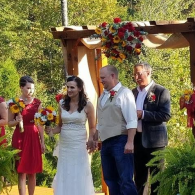 Wedding couple and attendants standing under a flower-decorated wooden arch outdoors