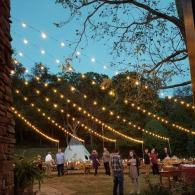 String lights over a backyard party with people gathered around tables at dusk