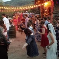 People dancing at an outdoor evening festival with string lights and warm lantern glow