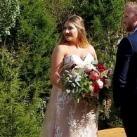 Bride in a lace wedding dress holding a bouquet of white and red flowers outdoors