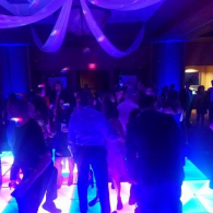 People dancing on a glowing blue-purple dance floor at a dimly lit party