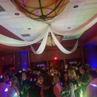 Crowded indoor dance floor with colorful lights and white draped ceiling decor at a party