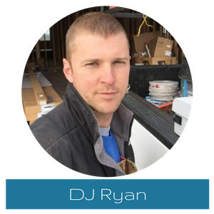 Portrait of DJ Ryan in a garage, wearing a dark jacket over a blue shirt