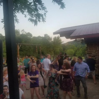 Group of people mingling outdoors at a backyard gathering near a house and trees at dusk