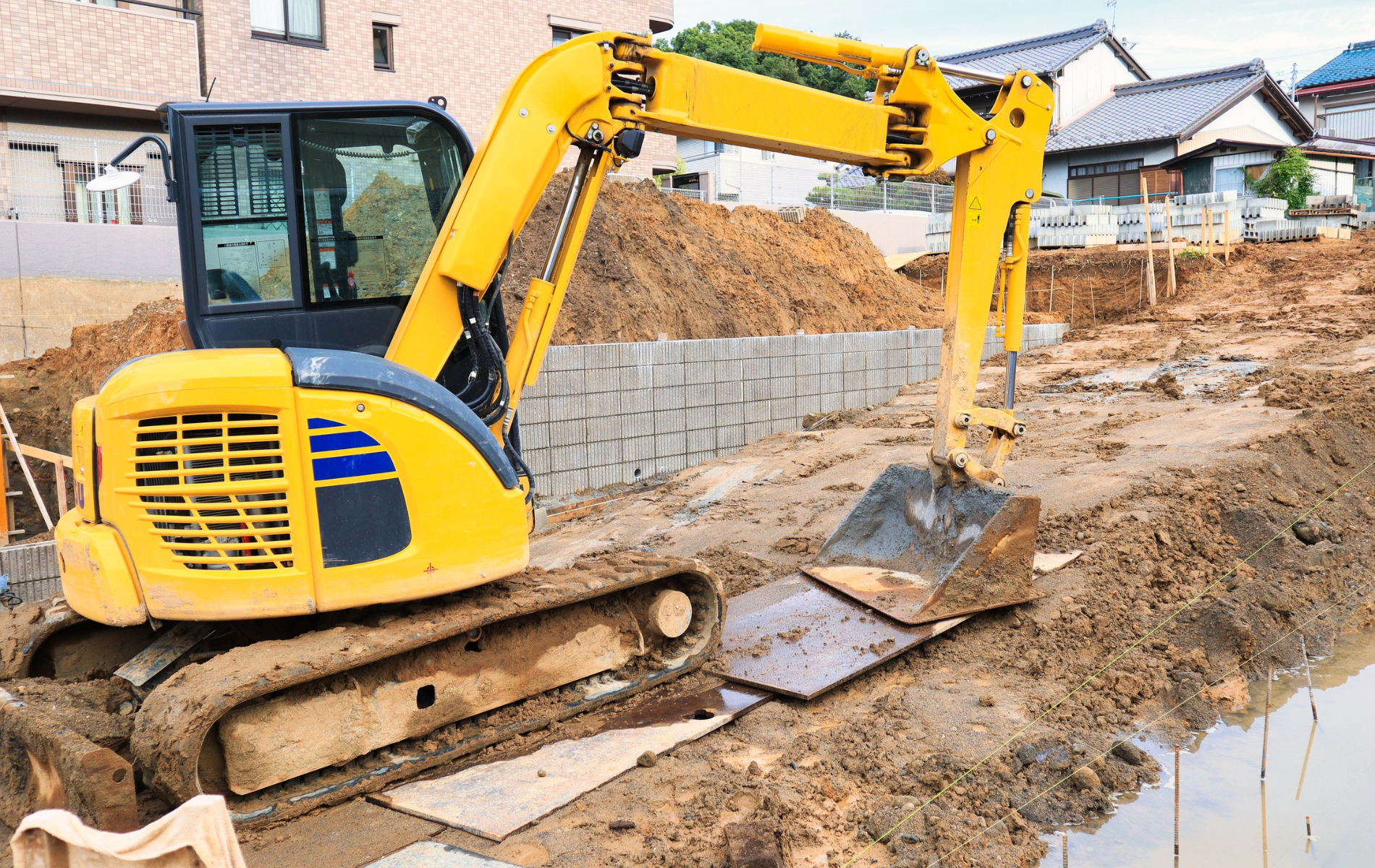 Yellow excavator digging earth at a construction site near homes